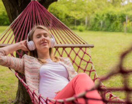 Woman with earphones is lying down on hammock