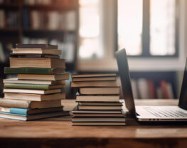 Organized pile of books on a desk with a laptop